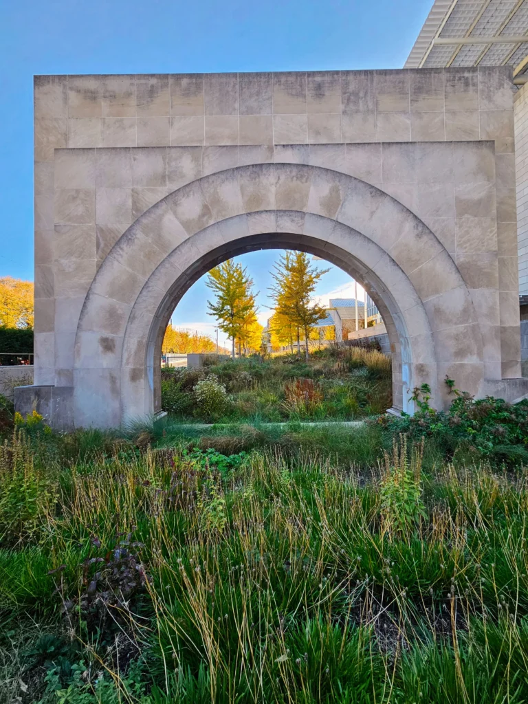 Simple arch on a patch of grass with yellowing trees in the distance as seen through the arch.