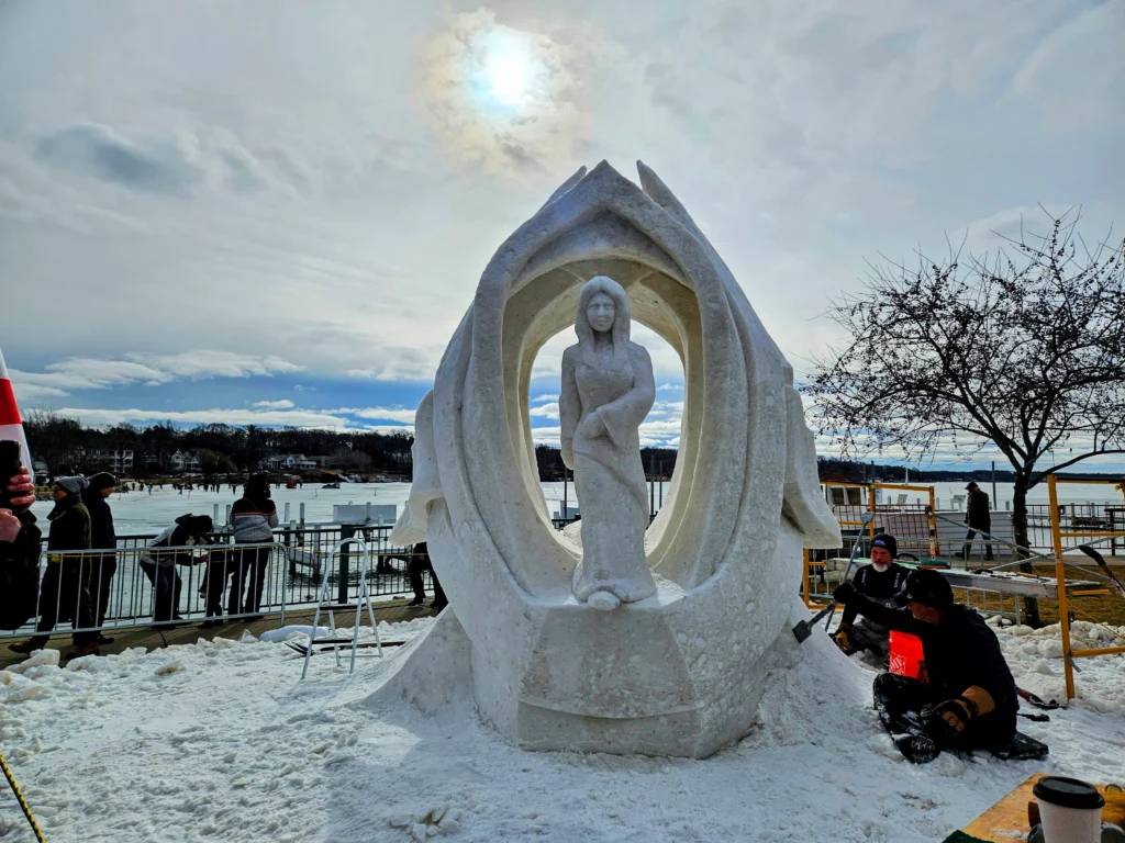 Snow sculpture of woman in long robe under an arch.